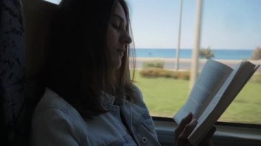 Otobüsle seyahat ve kitap okuma genç kadın. Kız pencerenin önünde arabada seyahat