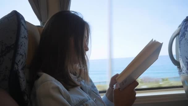 Mujer joven viajando en autobús y leyendo libro. Chica está viajando en el coche delante de la ventana — Vídeos de Stock