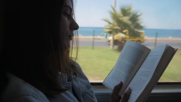 Jonge vrouw reizen per bus en te lezen boek. Meisje is reizen in de auto voor het raam — Stockvideo