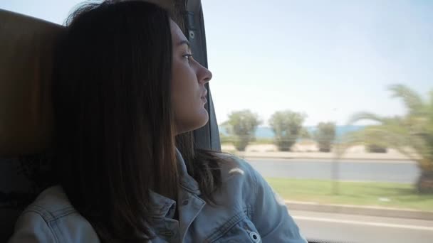 若いブルネットの女性、バスの旅の窓から景色を眺めながら — ストック動画