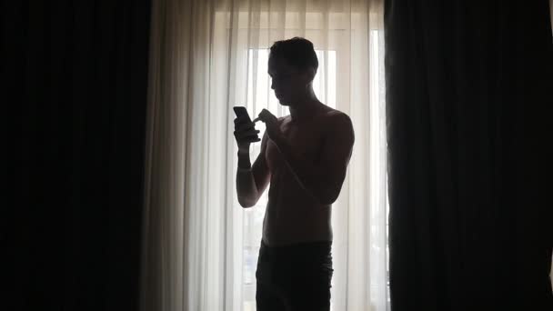 Молодой человек пишет смс на смартфоне у себя дома — стоковое видео