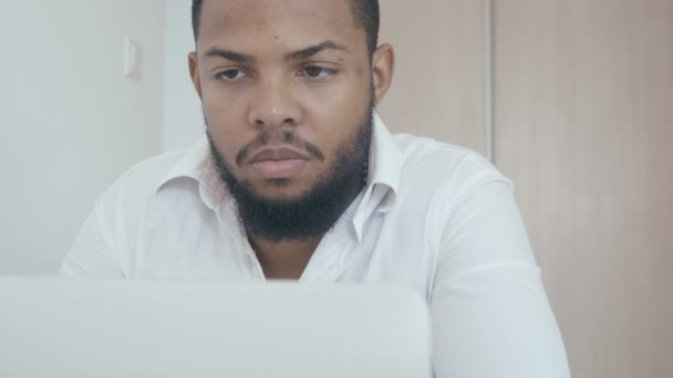 Серьезный чернокожий человек, работающий с компьютером, смотрит на монитор в офисе. Африканский бизнесмен работает за ноутбуком . — стоковое видео