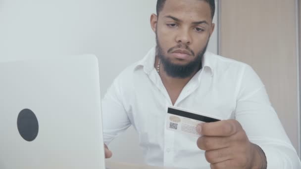 Africano joven de compras en línea con tarjeta de crédito utilizando el ordenador portátil en casa . — Vídeo de stock