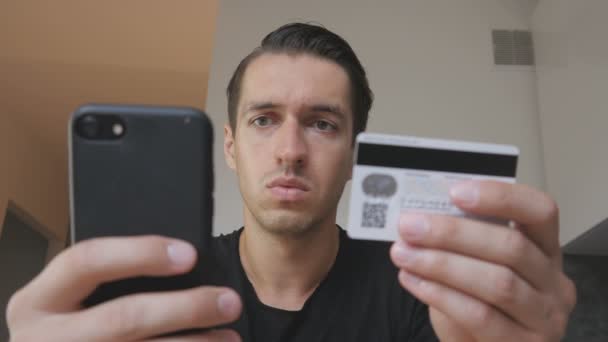 Злой молодой человек, покупающий онлайн, пользуется телефоном и кредитной картой и чувствует, что его обманули. Неудачные интернет-покупки. Мошенничество с кредитной картой — стоковое видео