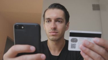 Mutlu genç adam online kullanır satın alma bir telefon ve bir kredi kartı evde mutfak alışveriş internet kullanır smartphone