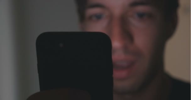 Közelről használ smartphone dart szoba otthon fiatalember. . Elmélkedés a smartphone, az arcán — Stock videók