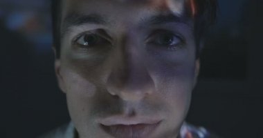 Genç adam bir video ya da Tv veya bilgisayar monitörü evde film izlerken kapatın. Onun yüzünde yansıma.