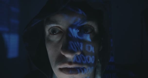 Close up of Crazy hacker programmer in hood with binary code reflection on his face in dark room at night. Portrait of dangerous Mad man programmer. — Stock Video