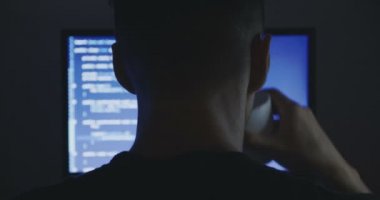 Programcı inşaat üstünde yeni bir program deneyimli. Genç adam hacker karanlık oda, yazılım kaynak kodu yazıyor ve kahve içiyor. Arkadan görünüm.