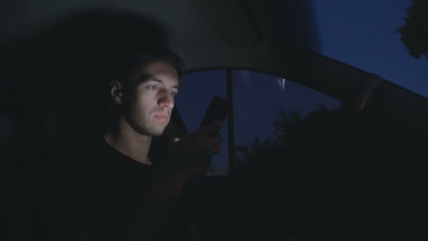 Fiatal ember használ egy okos telefon, egy autó az úton, a város éjszakai ülve — Stock videók