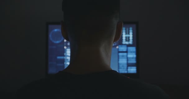 Чоловічий хакер працює на комп'ютері з картами та даними на екрані в темній офісній кімнаті . — стокове відео