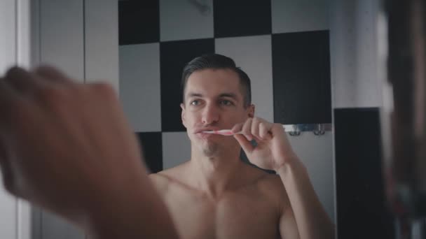 El joven se cepilla los dientes en el baño por la mañana. Cuidado de los dientes . — Vídeos de Stock