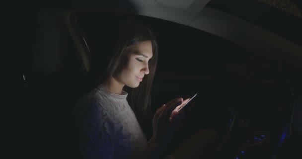 Schöne Frau, die nachts mit Smartphone im Auto sitzt. — Stockvideo