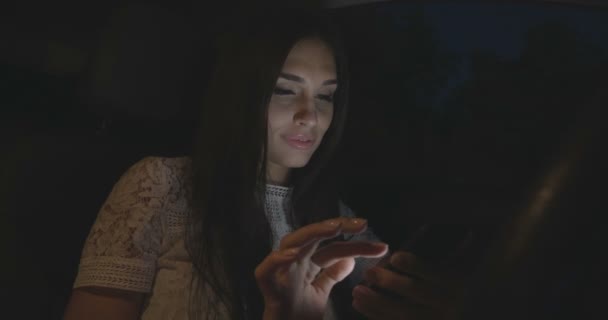 Beautiful woman sitting in the car using smartphone at night. — Stock Video