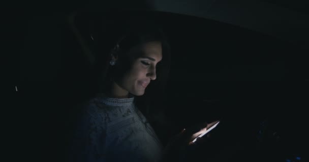 Mooie vrouw zitten in de auto met behulp van smartphone's nachts. — Stockvideo