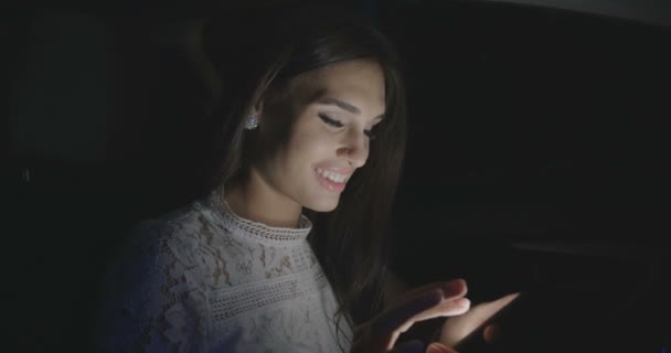 Красива жінка сидить в машині, використовуючи смартфон вночі . — стокове відео