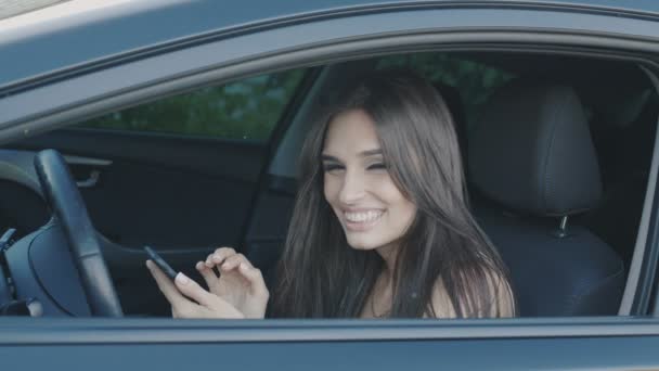 若いブルネットの女性は、車に坐っている間スマート フォンを使用してください。 — ストック動画