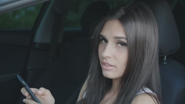 Joven morena mujer utiliza un teléfono inteligente mientras está sentado en un coche — Vídeo de stock