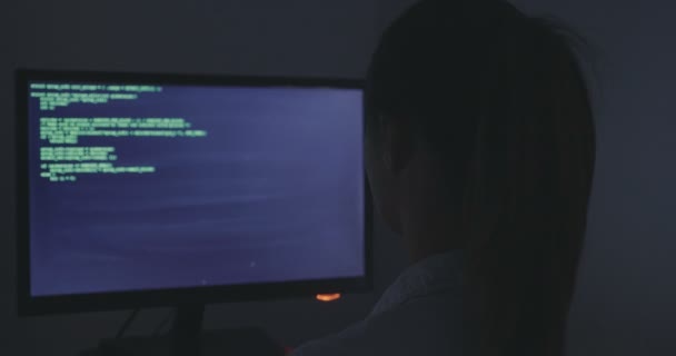 Zažila to žena programátor pracuje na novém programu. Mladá žena hacker píše zdrojový kód softwaru v temné místnosti. Pohled zezadu. — Stock video
