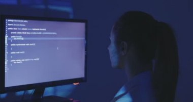 Kadın programcı inşaat üstünde yeni bir program deneyimli. Genç kadın hacker karanlık oda, yazılım kaynak kodu yazıyor. Arkadan görünüm.