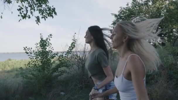 Dos amigas las mujeres corriendo a lo largo de la carretera a viajar. Rubia y morena sonriendo y divirtiéndose de vacaciones. Steadicam tiro — Vídeos de Stock