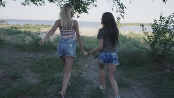 Due amiche donne che corrono lungo la strada in viaggio. Bionda e bruna che sorridono e si divertono in vacanza. Steadicam shot — Video Stock
