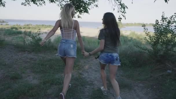 Két nő fut végig az út utazás. Blonde- és brunette mosolyogva és szórakozás a nyaralás. Steadicamnél lövés — Stock videók