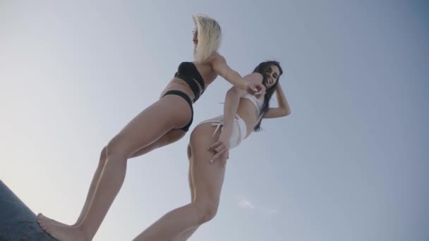 Zwei aktive und lustige Mädchen tanzen und scherzen im Freien vor Himmelshintergrund und posieren für die Kamera — Stockvideo