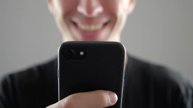 Portre, gülümseyen genç adam kullanarak Internet veya sosyal ağlar kontrol beyaz arka plan üzerinde tarama Smartphone,