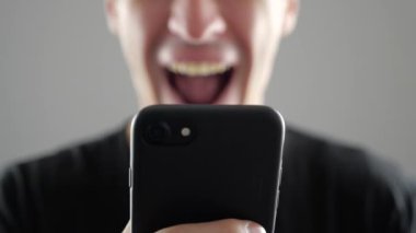 Portre, gülümseyen genç adam kullanarak Internet veya sosyal ağlar kontrol beyaz arka plan üzerinde tarama Smartphone,