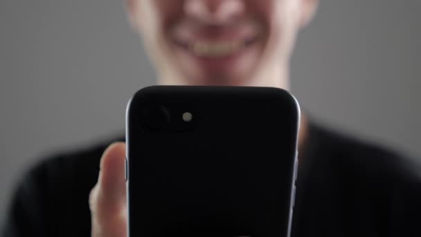 Primo piano del giovane uomo sorridente che utilizza smartphone, naviga in Internet o controlla i social network su sfondo bianco — Video Stock