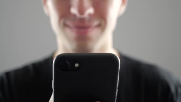 Primo piano del giovane sorridente che utilizza smartphone, naviga in Internet o controlla i social network su sfondo bianco — Video Stock