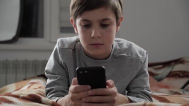 Çocuk çocuk cep telefonu ile evde oynamak. Çocuk bir yatakta yatarken Smartphone kullanarak