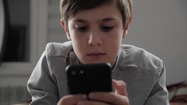 Menino brincando com celular em casa. Kid Usando Smartphone enquanto deitado em uma cama — Vídeo de Stock