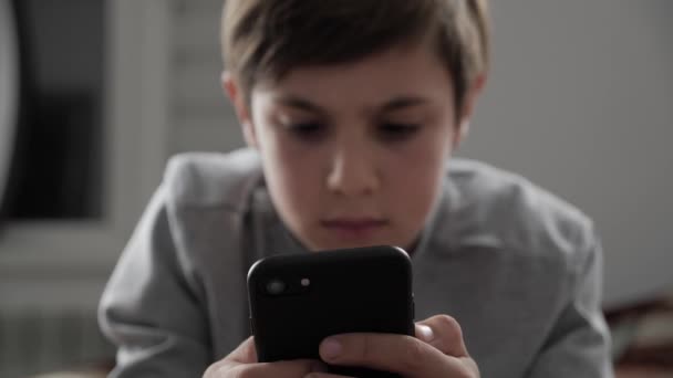 携帯電話を家で遊んで子供男の子。ベッドの上に横たわっている間子供を使用してスマート フォン — ストック動画