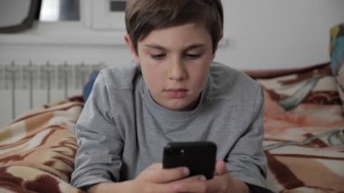 Çocuk çocuk cep telefonu kulaklık ile birlikte evde oynamak. Çocuk bir yatakta yatarken Smartphone kullanarak