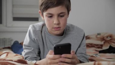 Çocuk çocuk cep telefonu kulaklık ile birlikte evde oynamak. Çocuk bir yatakta yatarken Smartphone kullanarak