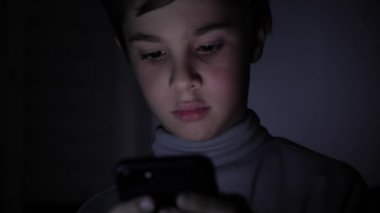 Mutlu çocuk heyecanla evde karanlıkta bir oyunda bir akıllı telefon üzerinde çalış. Çocuğun yüzü parlak bir İzleyicisi tarafından yaktı