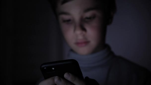 Primer plano de la cara de niño feliz joven mirando el teléfono inteligente en la noche en casa — Vídeo de stock