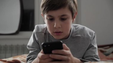 Çocuk çocuk cep telefonu ile evde oynamak. Çocuk bir yatakta yatarken Smartphone kullanarak