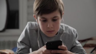 Çocuk çocuk cep telefonu kulaklık ile birlikte evde oynamak. Çocuk bir yatakta yatarken Smartphone kullanarak