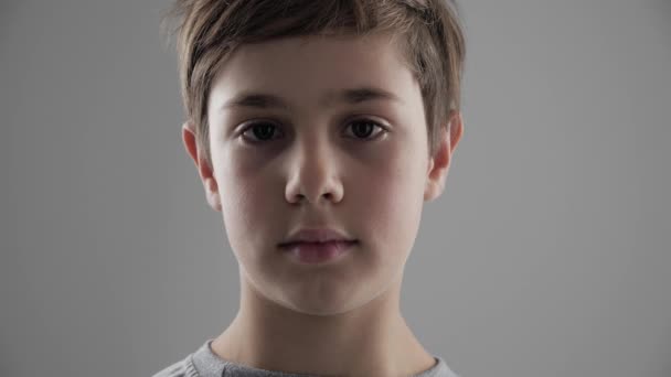 Портрет милого молодого хлопчика 11-12 років, який дивиться на камеру на білому тлі — стокове відео