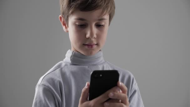 Porträt eines kleinen Jungen mit Smartphone auf weißem Hintergrund. Junge platziert Spiele auf Smartphone. — Stockvideo