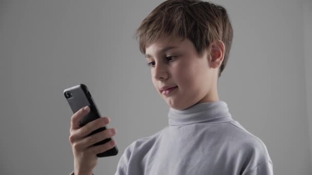 Retrato de niño pequeño usando Smartphone sobre fondo blanco. Chico trenzado juegos en el teléfono inteligente . — Vídeo de stock