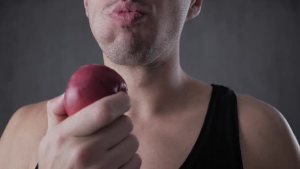 Gros plan du jeune homme qui mange de la pomme rouge à la maison dans la cuisine. Portrait de gars mangeant une pomme fraîche et regardant la caméra . — Video