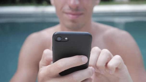attraktiver und gutaussehender junger Mann sieht aus, blättert durch Social-Media-Feeds auf dem Smartphone, während er sich im Urlaub am Pool ausruht