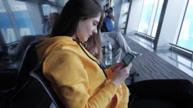 Havaalanında, yatılı için kadın beklemek Smartphone cep telefonu ile film izlerken zaman harcamak. Kulaklıklar bakmak için hareket eden aygıt perde ile kız