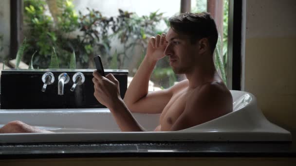 O homem deixa cair o telefone inteligente na água na banheira. Homem desleixado está faltando um smartphone na água no banheiro — Vídeo de Stock