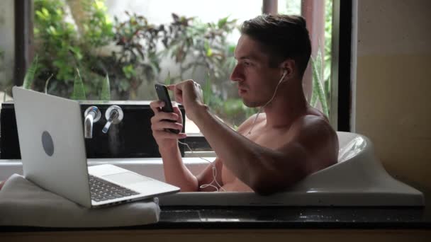Ocupado hombre de negocios multitarea se encuentra en el baño y funciona con un ordenador portátil y un teléfono inteligente — Vídeos de Stock