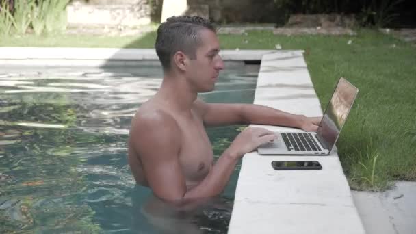 Podnikatel, pracovat na notebooku v bazénu. Chlap na volné noze pracuje na krásném místě v areálu u bazénu — Stock video
